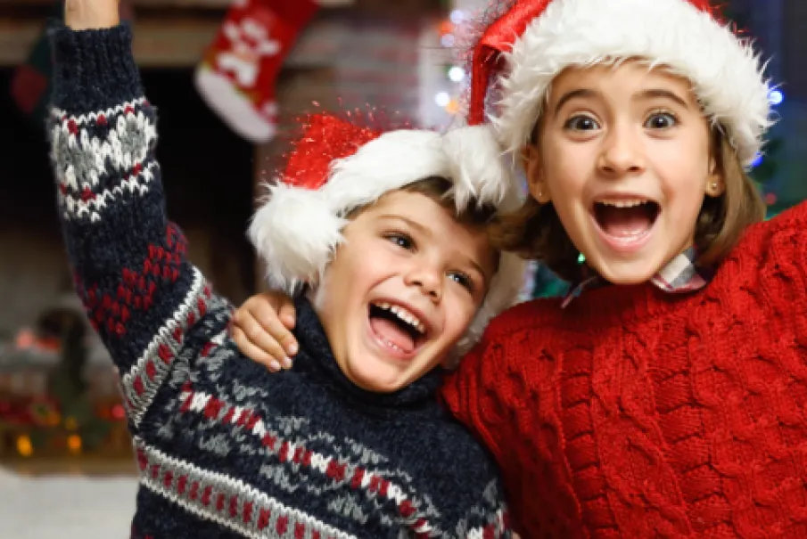Excited children wearing Santa hats in front of Christmas decorations.