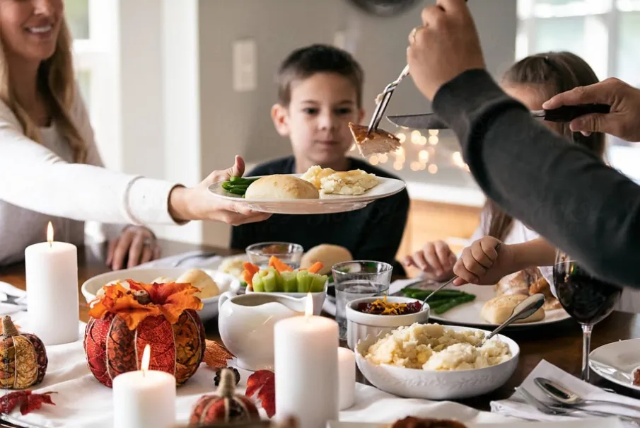 Family enjoying a festive meal with candles and autumn decorations on a dining table.