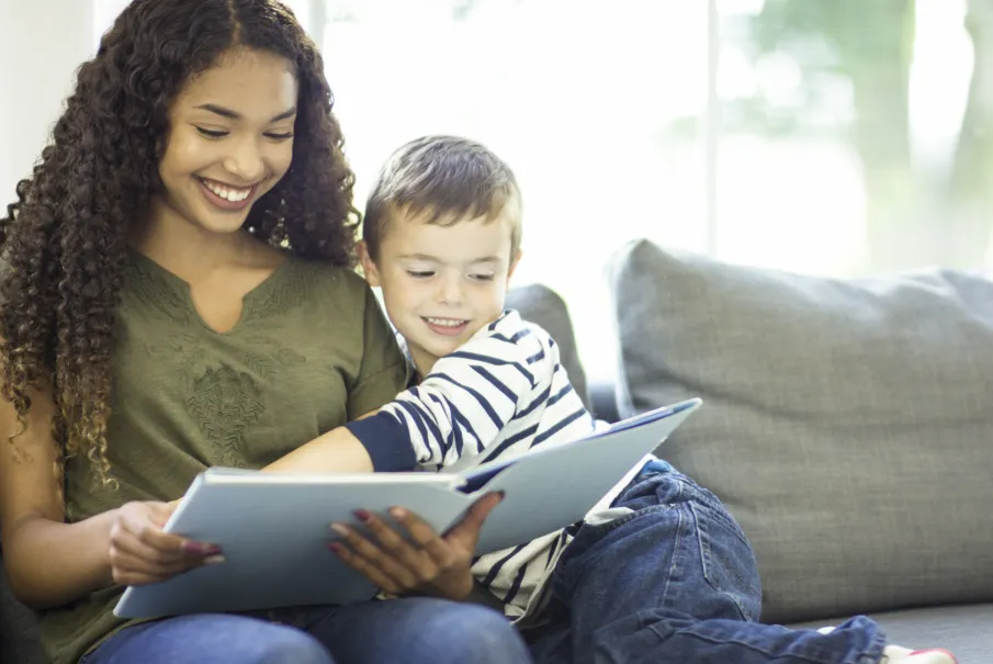 Smiling adult reading a book with a young boy on a couch