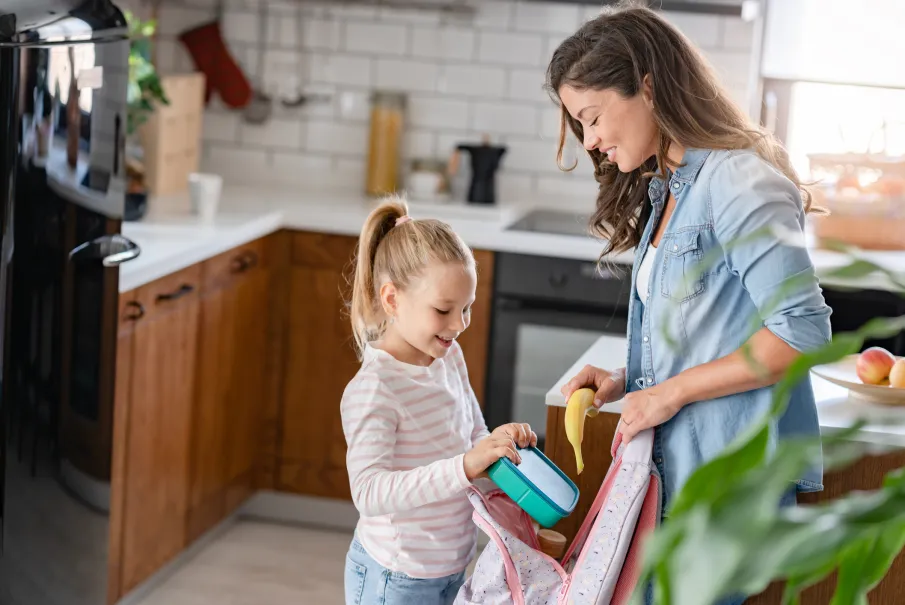 Woman and girl preparing a lunchbox in the kitchen for school.